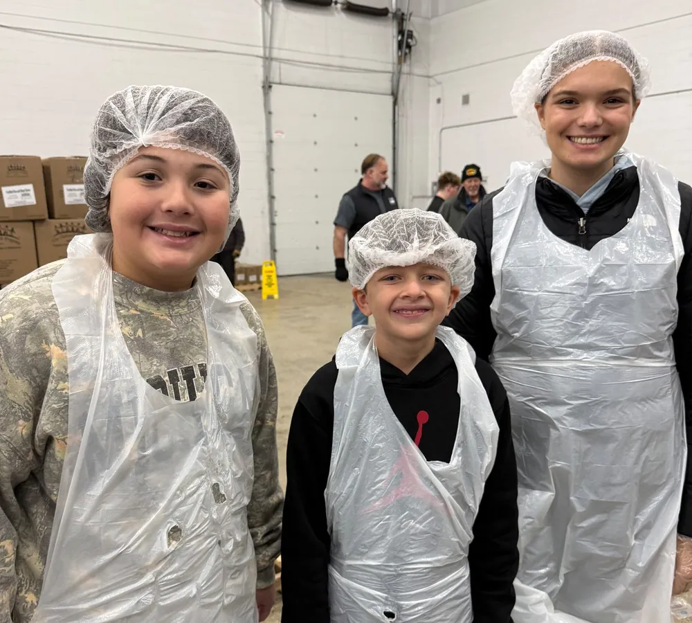 Young volunteers in hairnets and aprons packing food